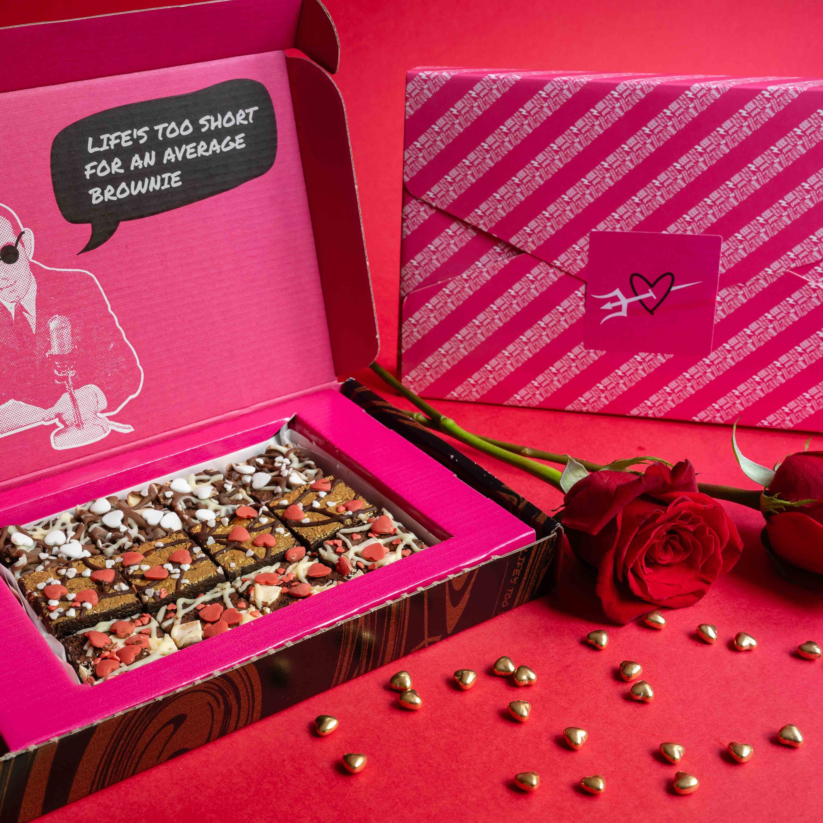 An open box of brownies with a gift wrapped box in the back, on a red background for Valentine's Day with scattered heart sprinkles and red roses