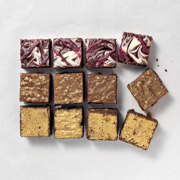A box of gourmet brownies with a variety of flavors, including salted caramel and cherry, arranged in a square pattern on a light background.