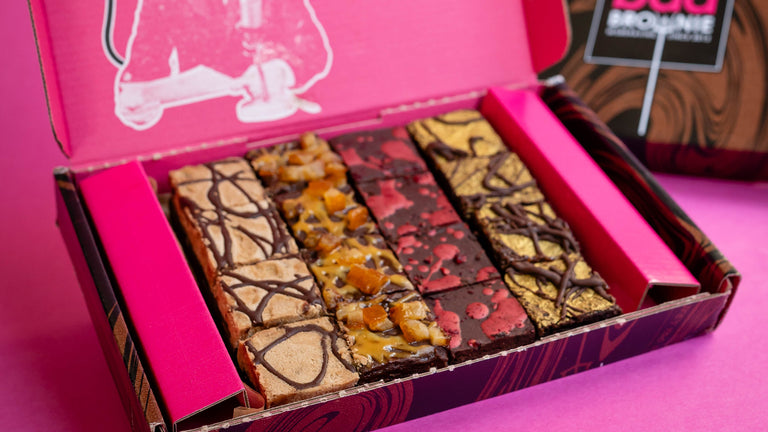 Open box of brownies with a pink lid featuring a cartoon character and text, on a pink background.