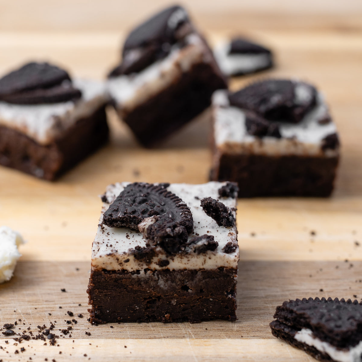 Oreo brownies topped with cream and cookie crumbs, arranged on a wooden board 