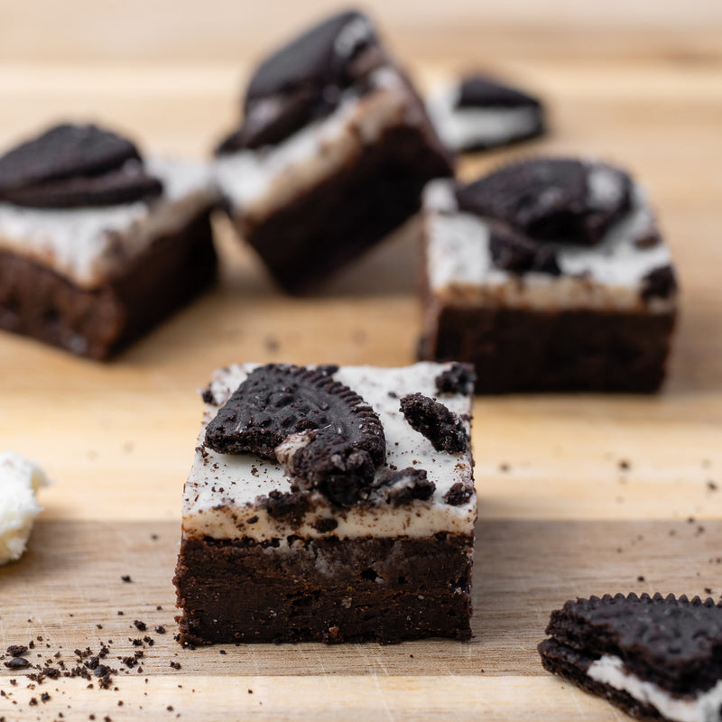 Oreo brownies topped with cream and cookie crumbs, arranged on a wooden board 