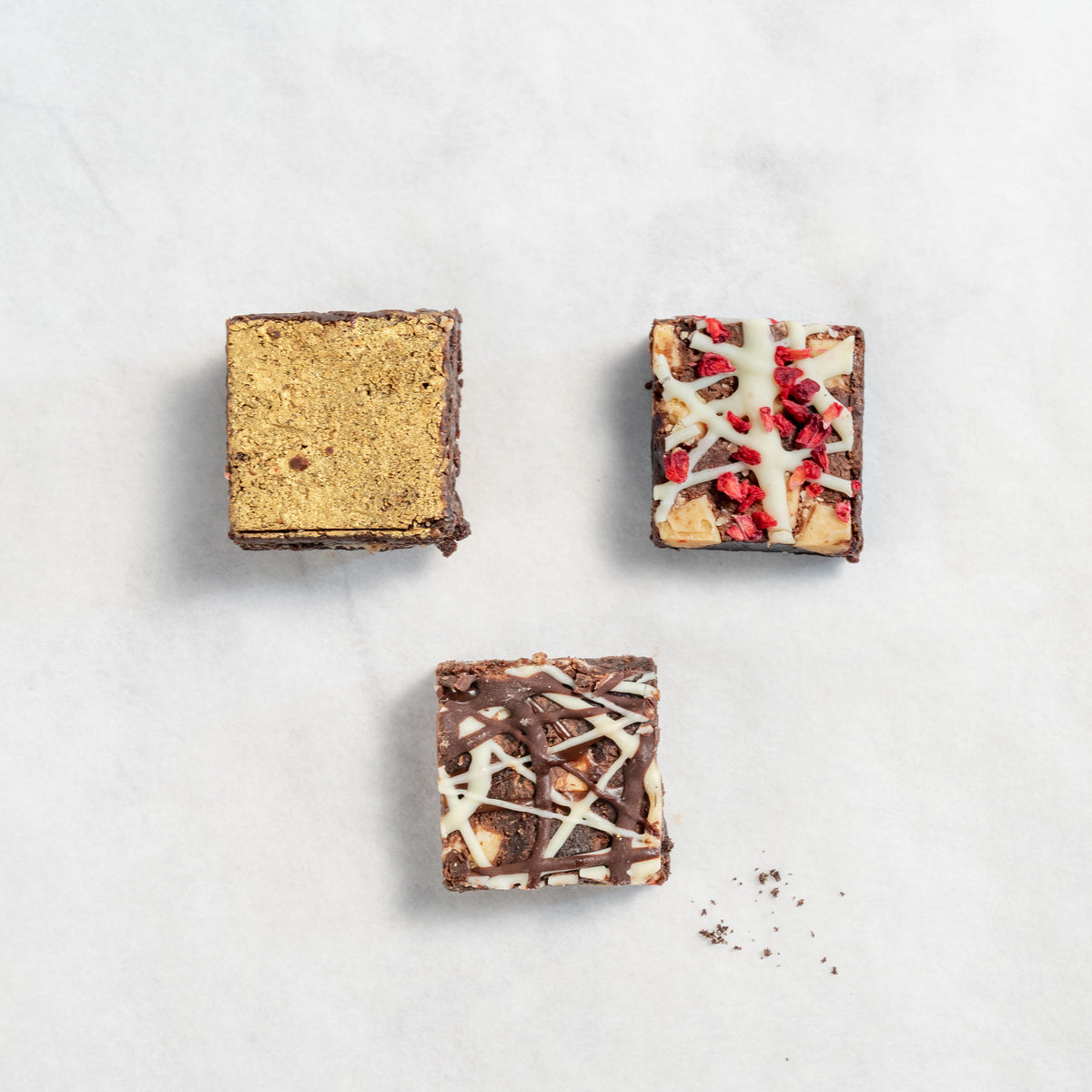 bite-sized brownies with different toppings and fillings, presented on a neutral background. contains salted caramel, triple chocolate and white chocolate raspberry brownies
