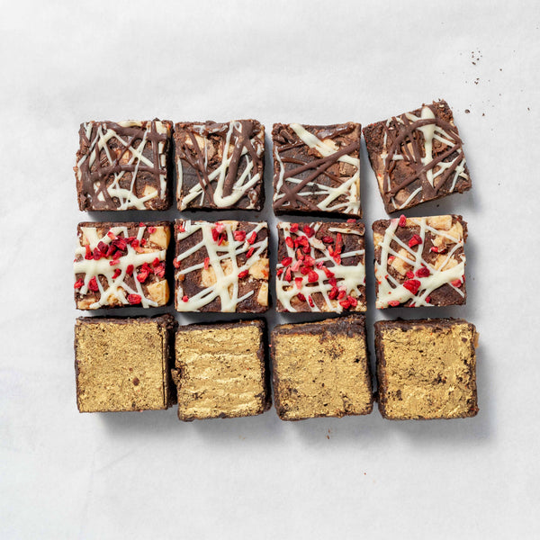 A box of assorted bite-sized brownies with different toppings and fillings, presented on a neutral background.