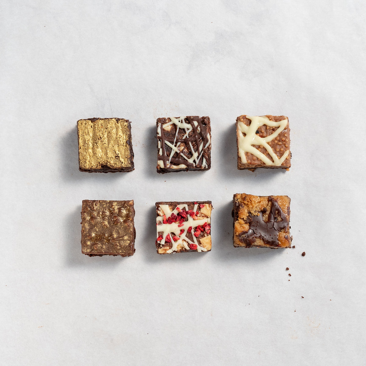 Top down view of 6 squares of flavoured chocolate brownies in 2 rows of 3 on white background