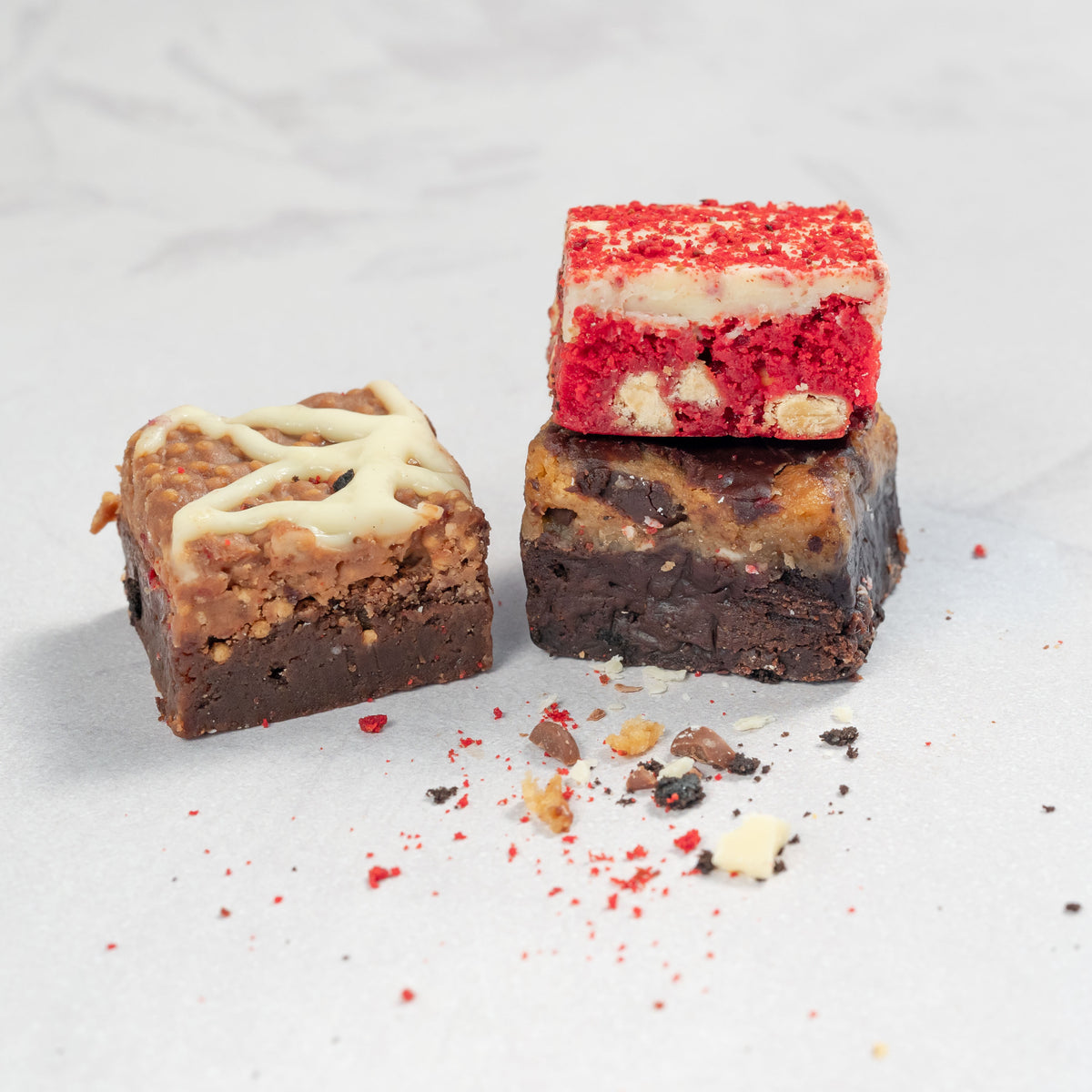 A close up image of assorted brownies with different toppings and fillings, stacked on top of each other