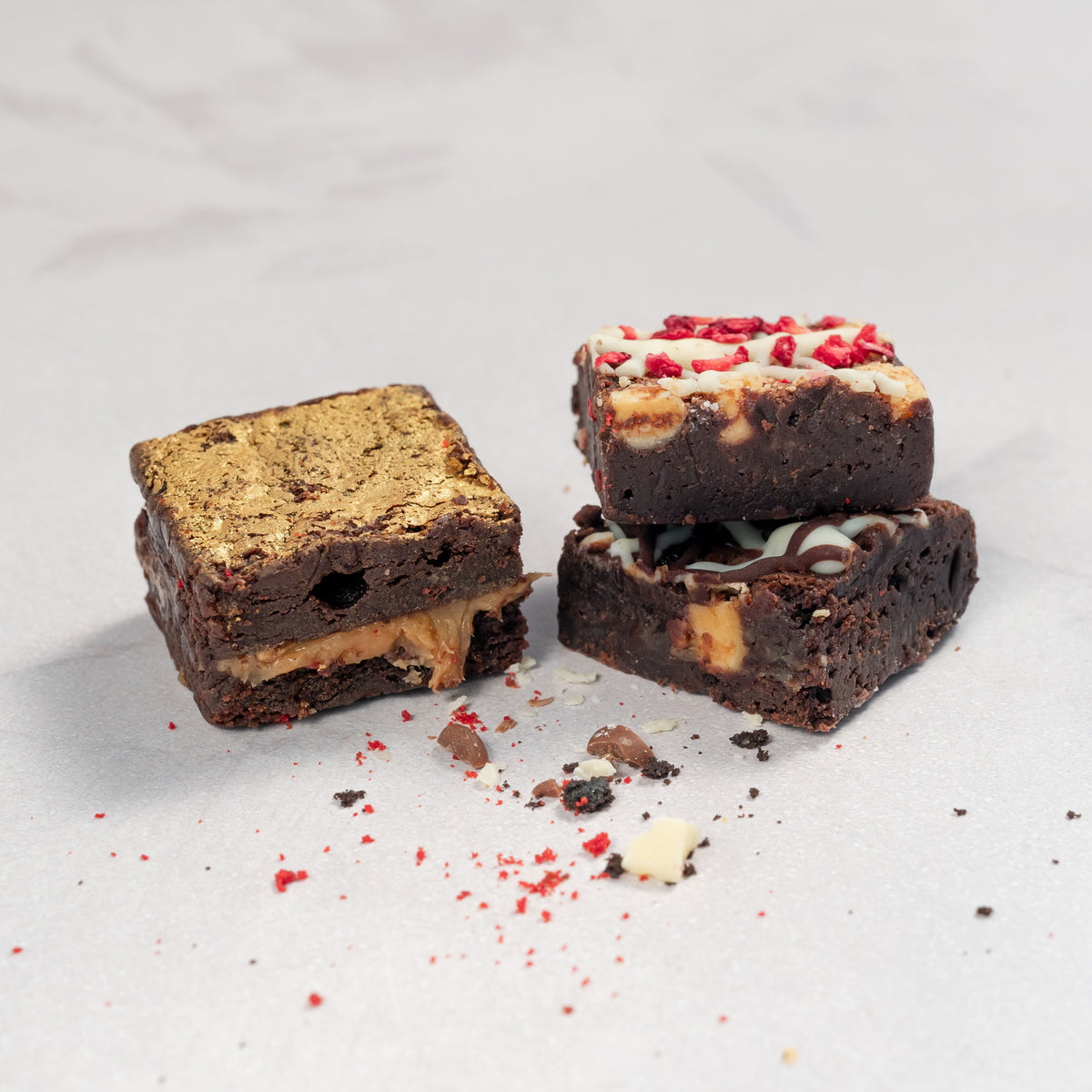bite-sized brownies with different toppings and fillings, presented on a neutral background. contains salted caramel, triple chocolate and white chocolate raspberry brownies