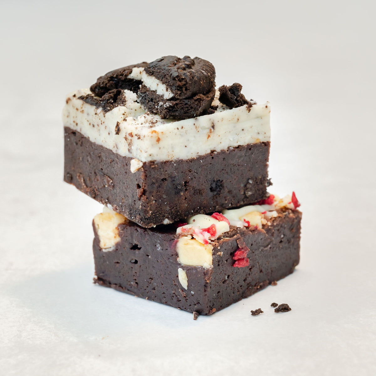 raspberry white chocolate brownie and Oreo cookies and cream brownie stacked on top of each other on a neutral background