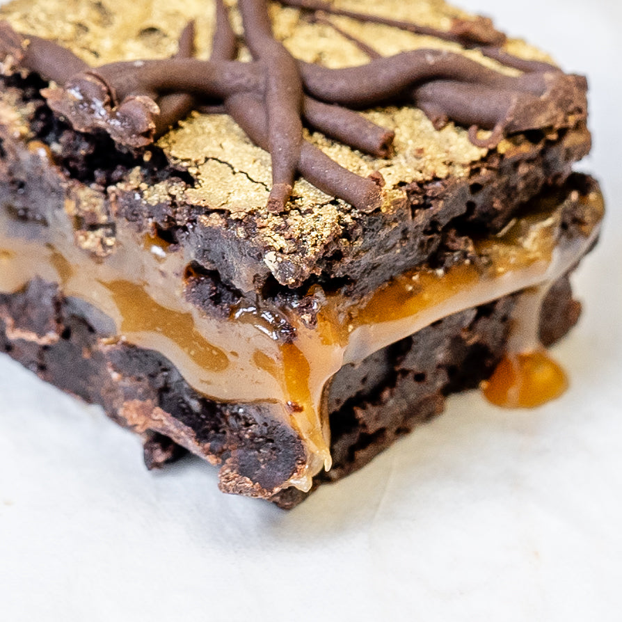 Close-up of a vegan and gluten free chocolate brownie with gooey salted caramel and chocolate drizzle on a white background