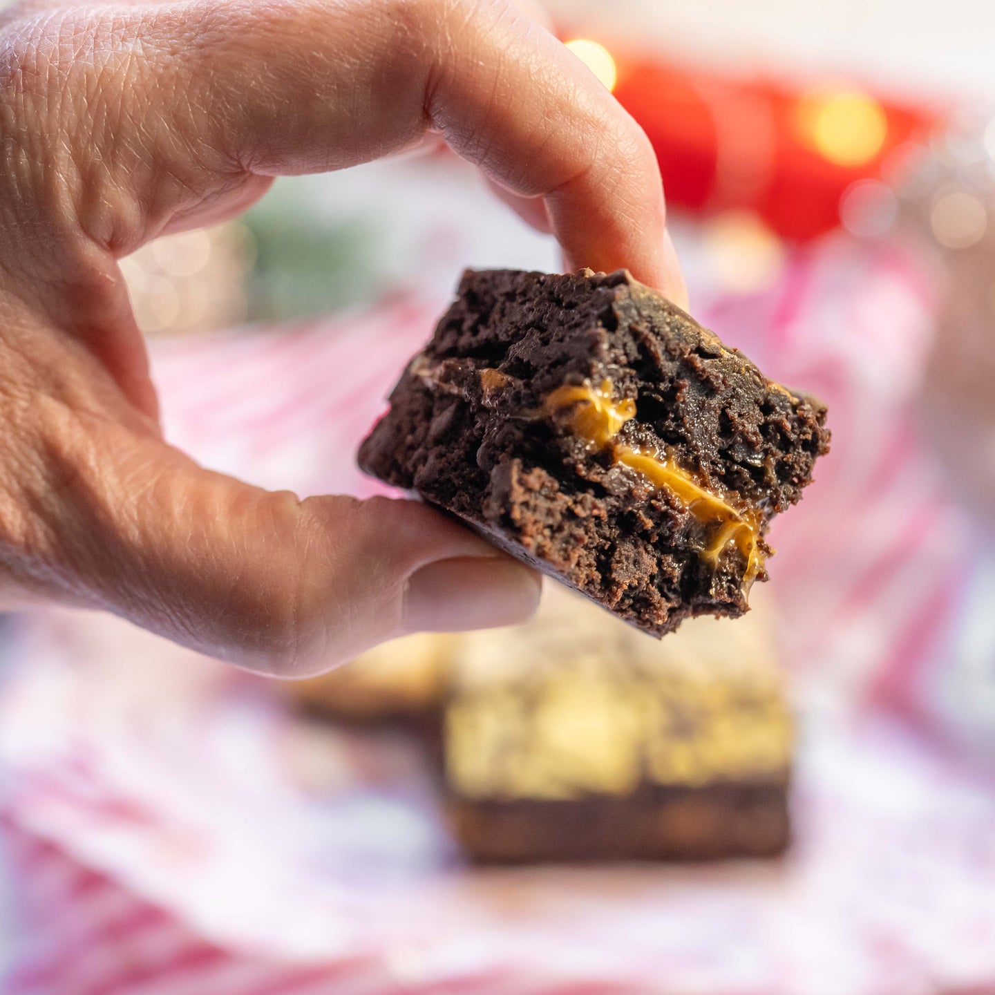 Chocolate brownie with salted caramel filling held by a hand against a blurred background