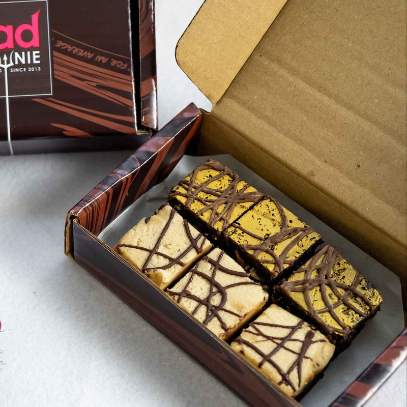 Box of assorted  vegan and gluten free chocolate brownies with a 'BAD BROWNIE' brand postal box on a white surface.