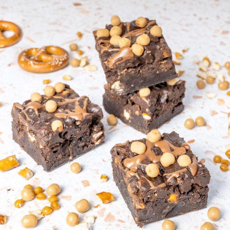 Chocolate brownie with pretzel pieces and salted caramel balls on a white surface