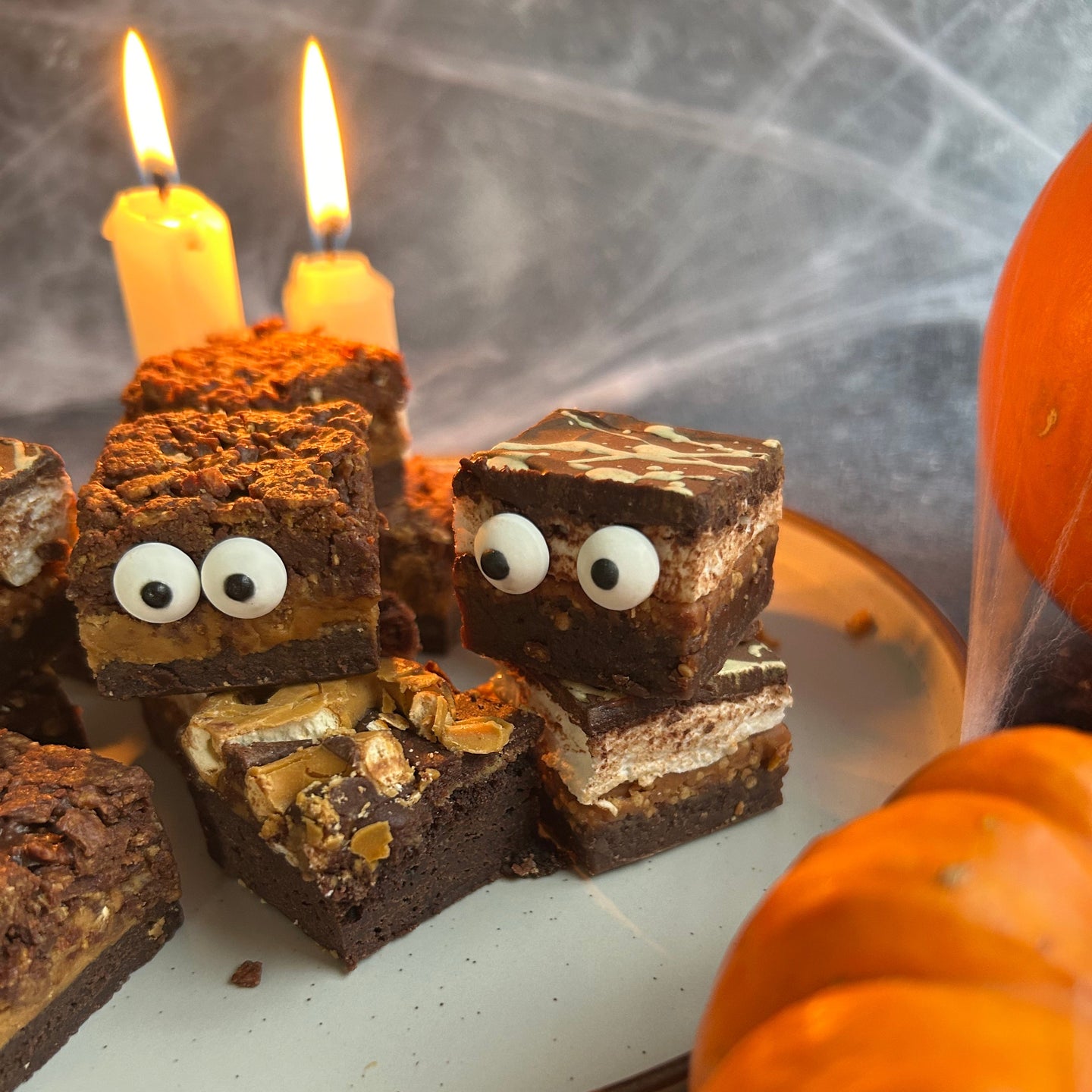 Brownie creature with candy eyes and legs on a plate with pumpkins in the background for Halloween