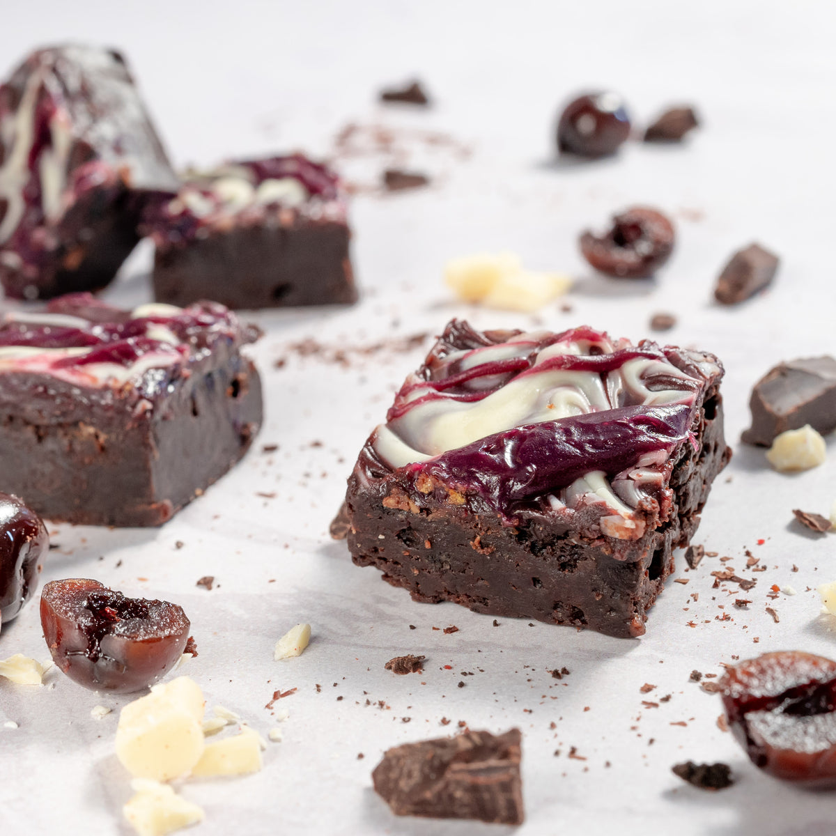 Close up photo of blackforest cherry flavoured dark chocolate brownies with cherries and chocolates scattered around