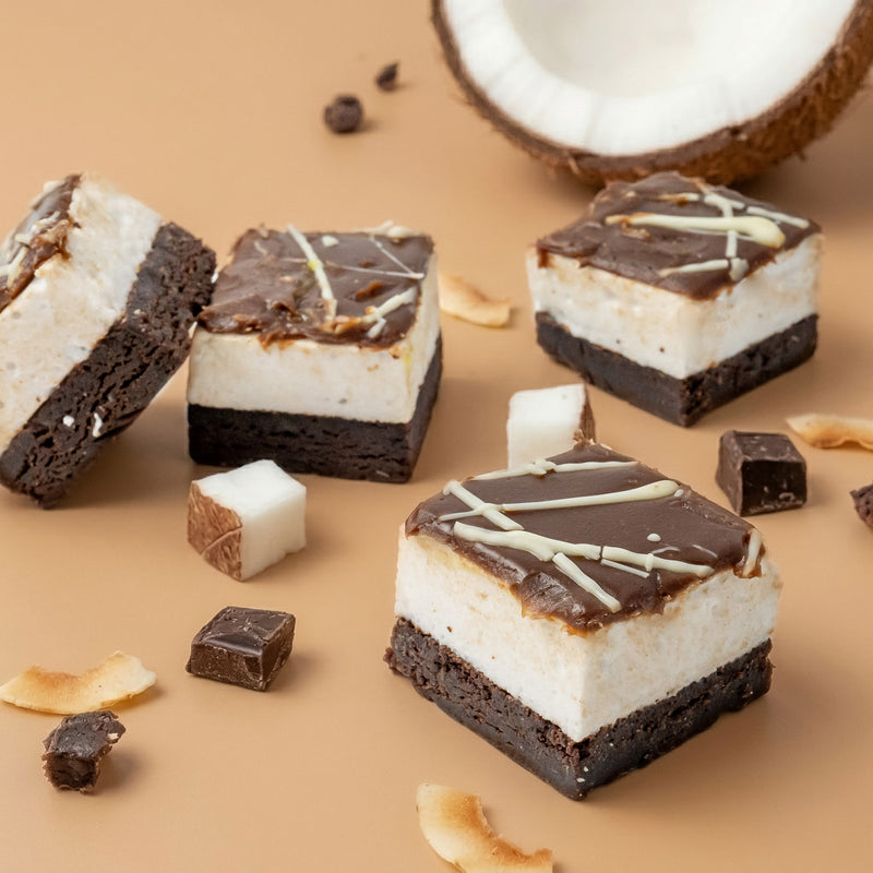toasted coconut marshmallow chocolate brownie on a white surface with a halved coconut in the background.