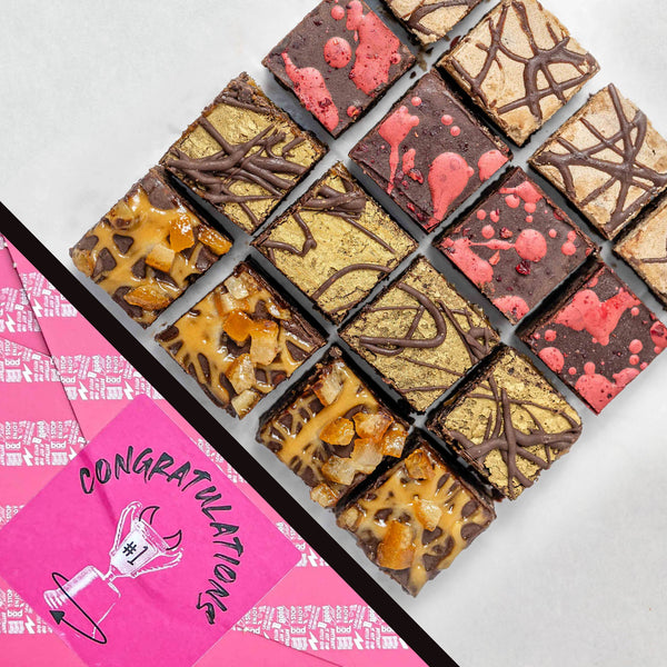 Can't Believe It's Vegan Wheat-Free 16 Bite Brownie Box in Congratulations gift wrap. Assorted brownies with different toppings on a white background, with a pink gift wrap reading 'Congratulations' partially visible.