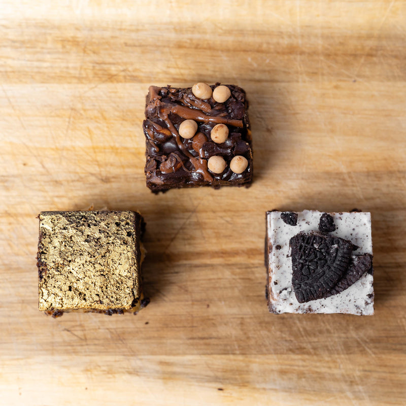 3 decorated brownie bites on a wooden board. FLavours are pretzel, cookies and cream, and salted caramel