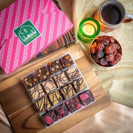 Assorted Eid vegan chocolate brownies on a wooden board with a pink box, cup of coffee, and bowl of dates.