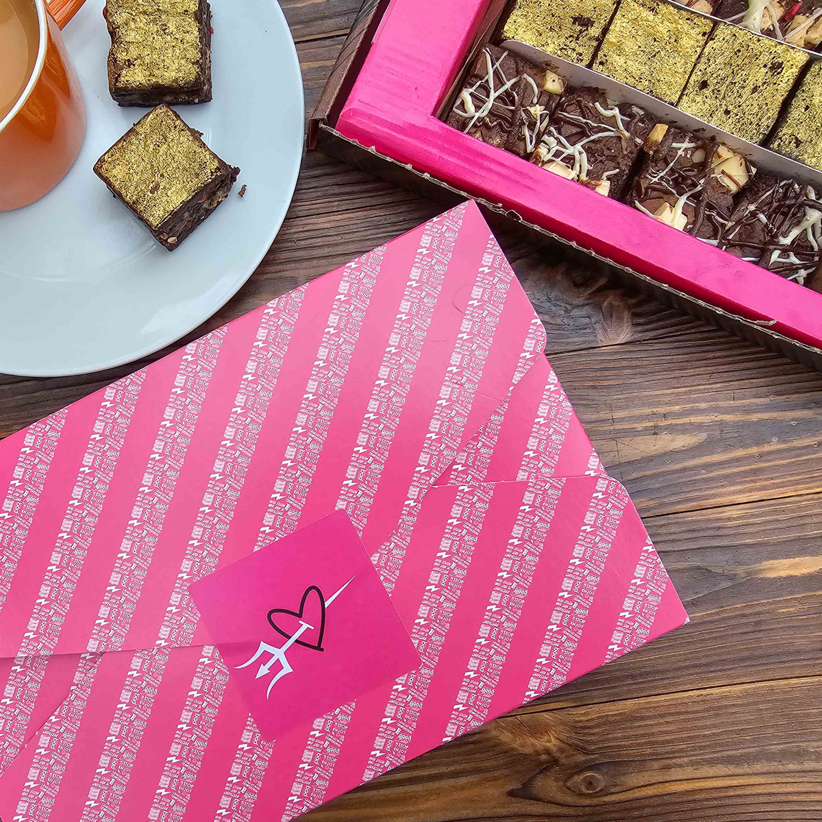 Pink gift wrap with a heart design on a wooden table with chocolate brownies and a cup of tea.