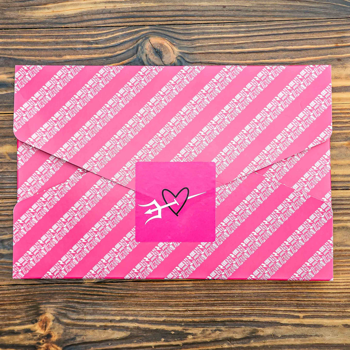 Pink gift wrapped brownie box with white diagonal stripes and a heart-shaped sticker on a wooden surface