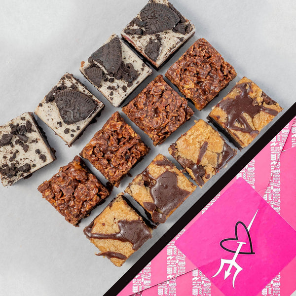 The Fully Loaded 12 Bite Brownie Box in Heart gift wrap. Assorted brownies on a gray surface with a pink bad brownie box featuring a heart.