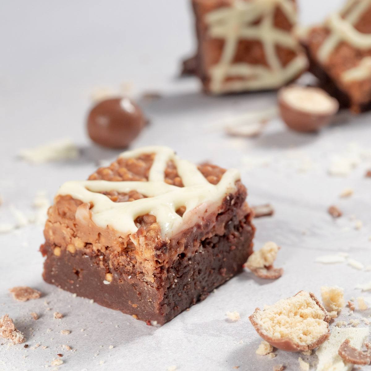 Close up photo of Maltesers chocolate brownies with a crunchy milk and white chocolate topping with maltesers and white chocolate scattered around
