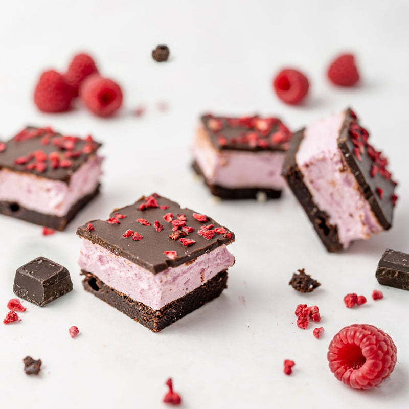 raspberry marshmallow chocolate brownie on a white surface with raspberries scattered around.
