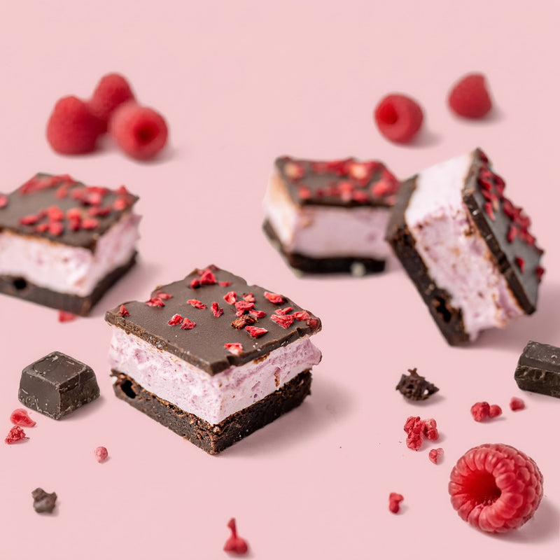 raspberry marshmallow chocolate brownie on a pink surface with raspberries scattered around.