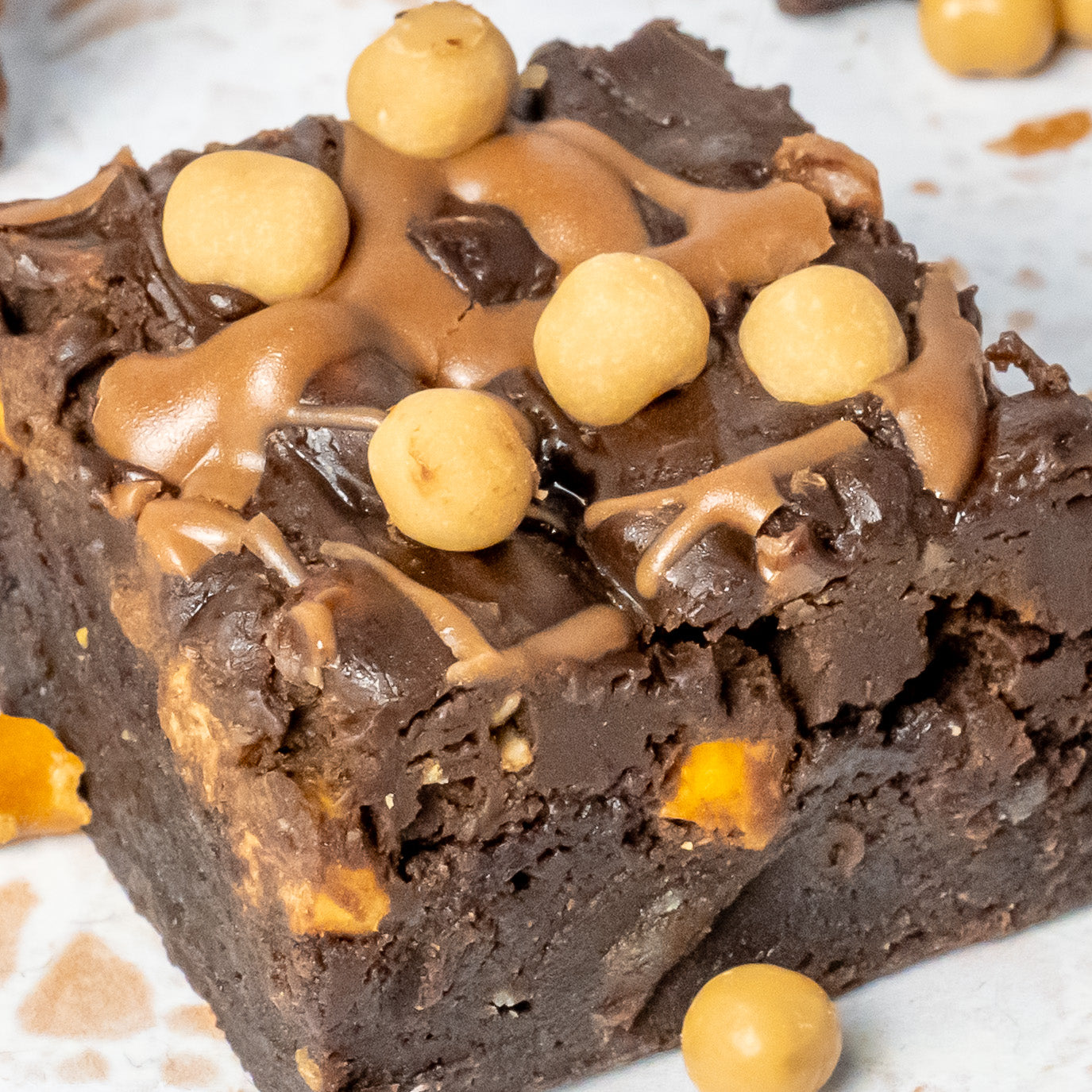 Chocolate brownie with pretzel pieces and salted caramel balls on a white surface
