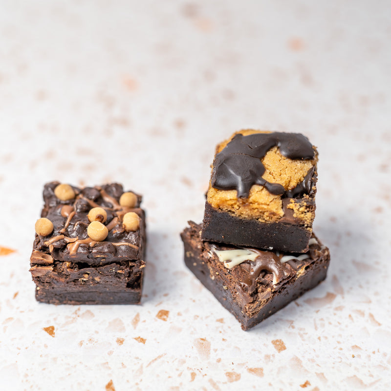 Three pieces of brownie with different toppings on a light background