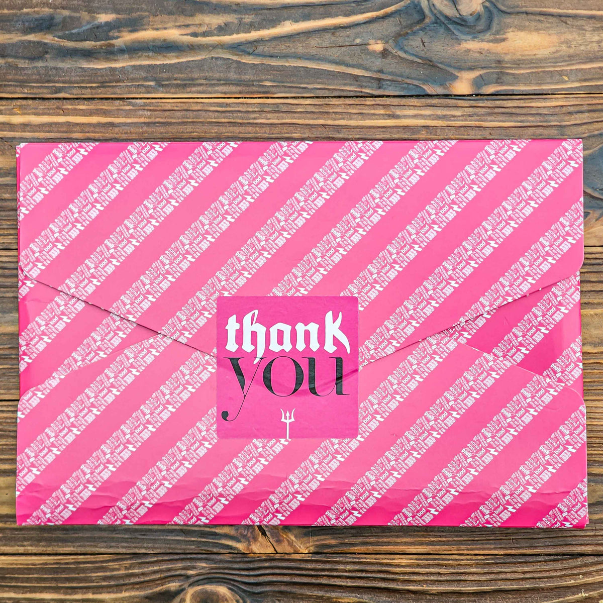 Pink gift wrapped bad brownie box with 'thank YOU' text on a wooden surface