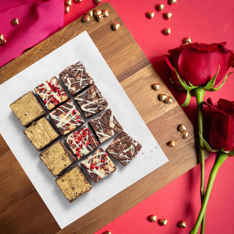 Assorted chocolate brownies on a wooden board with red roses on a red background