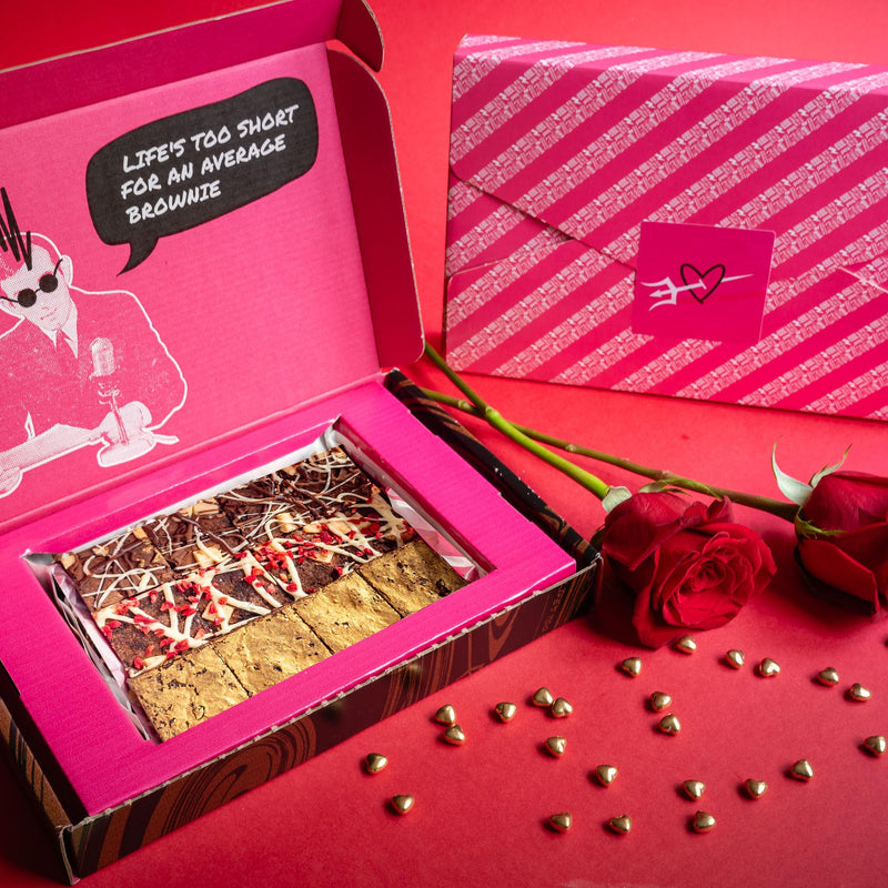 Open box of Bad Brownie chocolate brownies with a pink lid next to red roses on a red background.