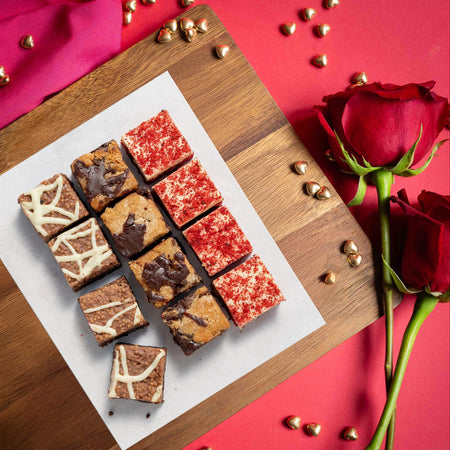 Assorted chocolate brownies on a wooden board with red roses on a red background for Valentine's Day
