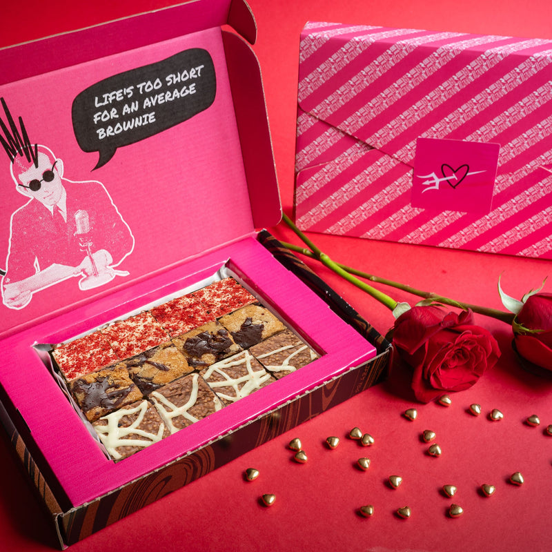 Open box of Bad Brownie chocolate brownies with a pink lid next to red roses on a red background.