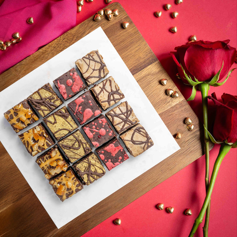 Assorted flavour vegan and gluten free chocolate brownies on a wooden board with red roses on a red background