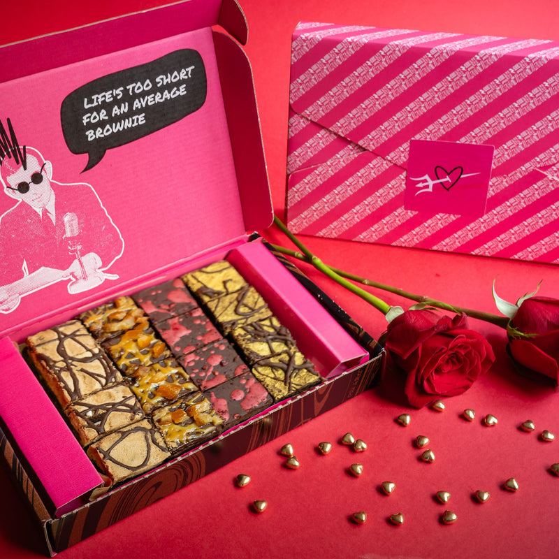 Open box of Bad Brownie vegan gluten free chocolate brownies with a pink lid next to red roses on a red background.