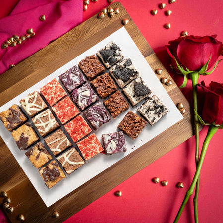 Assorted flavoured chocolate brownies on a wooden board with red roses on a red background