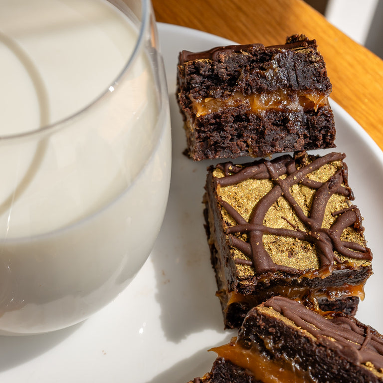Vegan brownies with salted caramel filling on a plate next to a glass of milk.